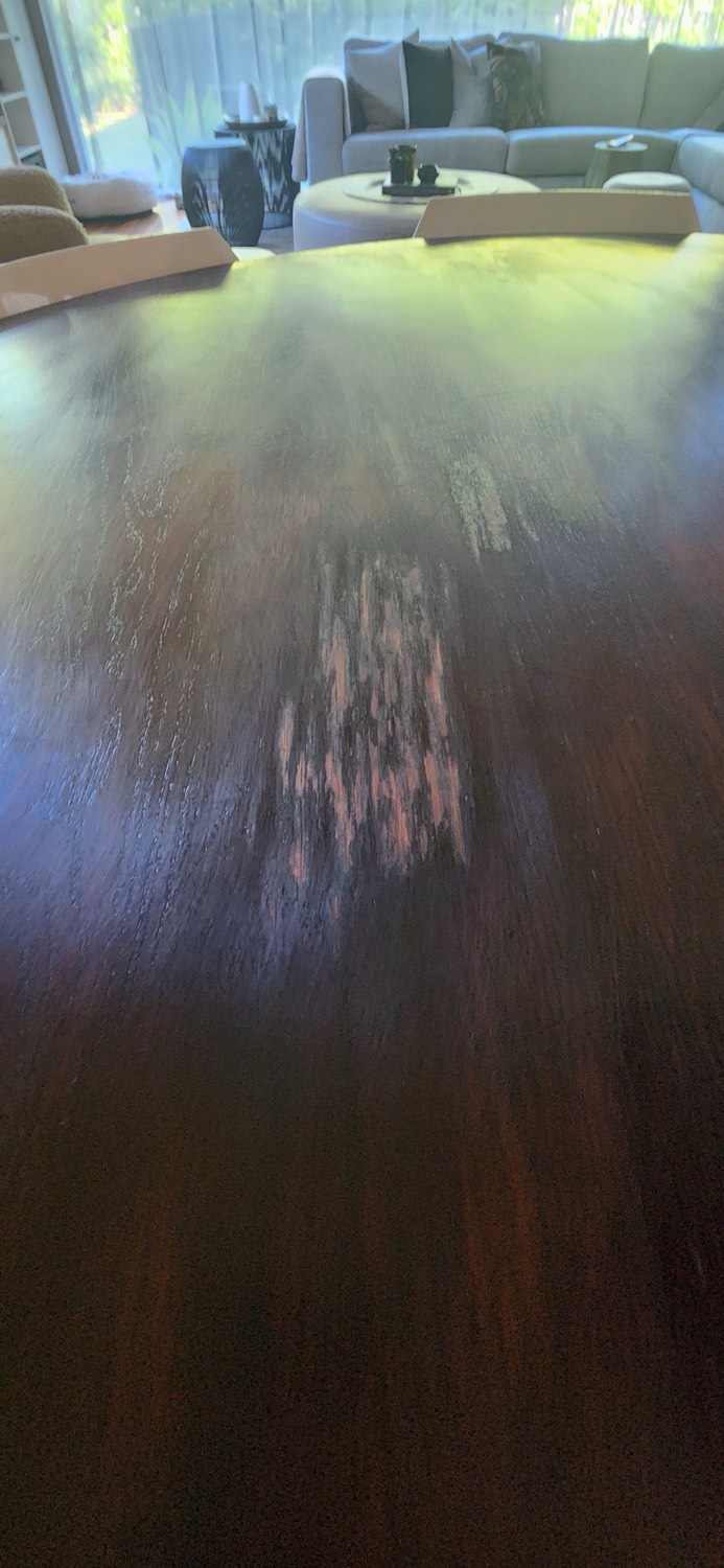 Close detail of acetone damage, streaked failed repair and water blooming on an oak dining table finish